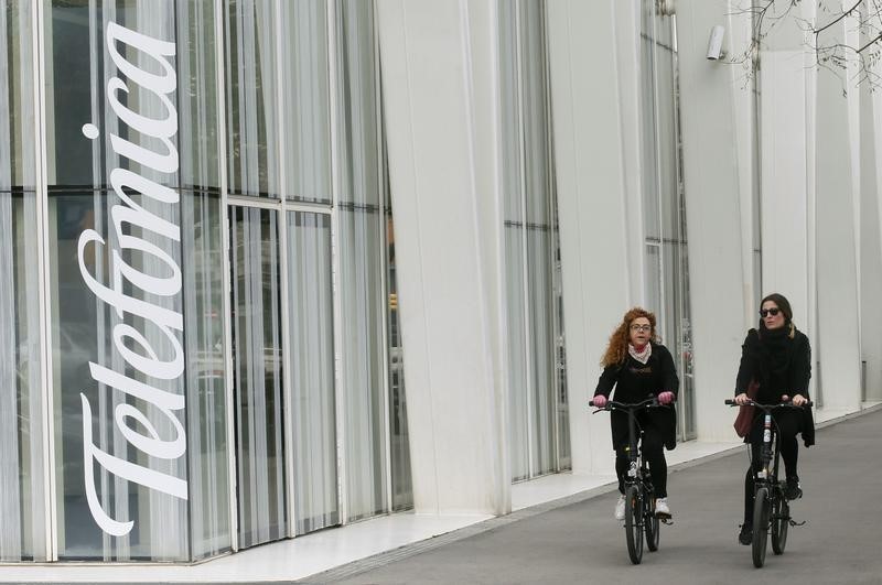 © Reuters. Women ride bicycles past the logo of Spain's Telefonica in Barcelona
