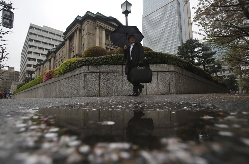 © Reuters. A man holding an umbrella walks past the Bank of Japan headquarters building as he is reflected in a puddle of water in Tokyo