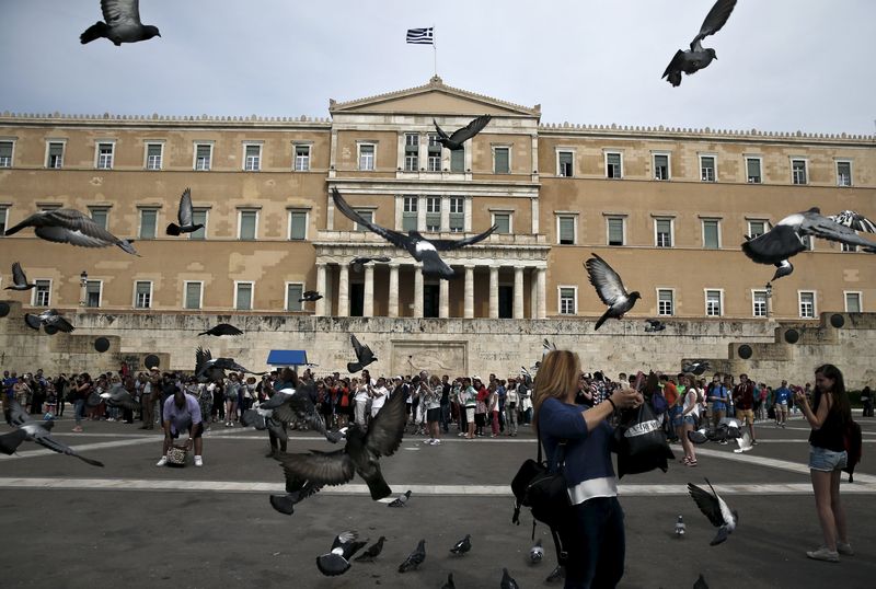 © Reuters. Tourists stand in front of the parliament building as pigeons fly by in Athens