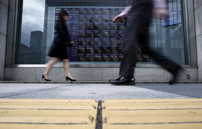 © Reuters. Pedestrians walk past an electronic board showing the various stock prices outside a brokerage in Tokyo