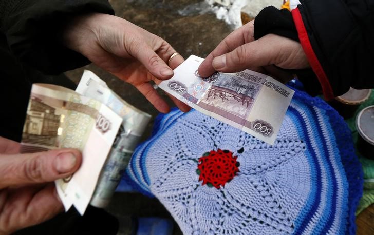 © Reuters. A vendor takes a Russian rouble banknote from a customer buying a handmade woolen rug in the village of Shoshino in Krasnoyarsk region