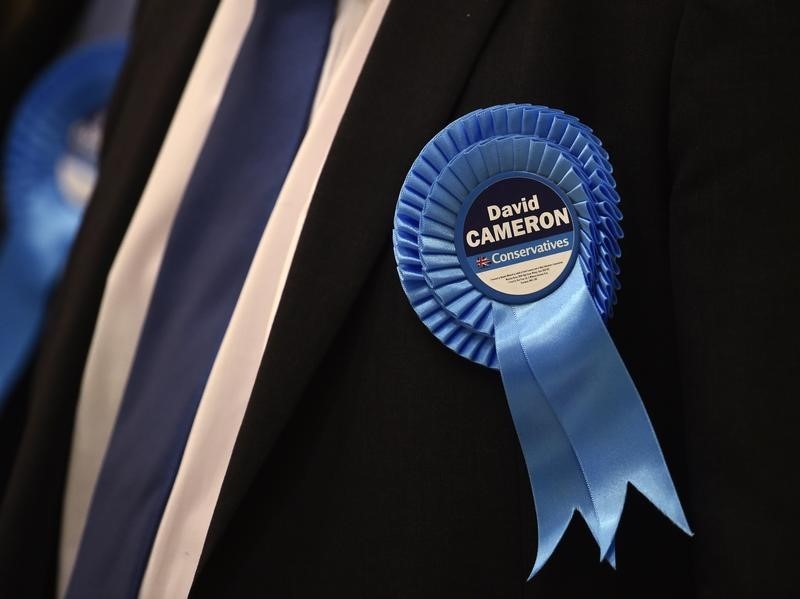 © Reuters. A Conservative party supporter wears a rosette in support of Prime Minister and local member of Parliament David Cameron at the counting centre, as votes are counted in Britain's general election, in Witney