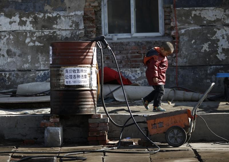 © Reuters. A boy walks past an oil barrel which is being used as a bucket at a car wash at a migrant workers' village in Beijing