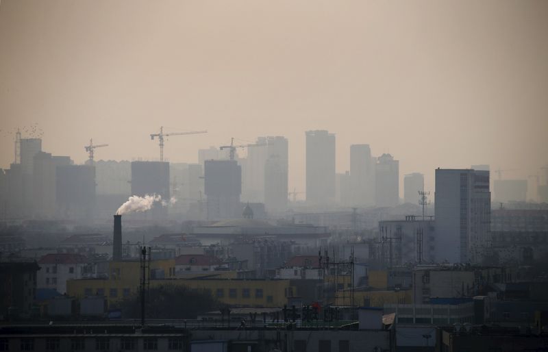 © Reuters. File photo of smoke rising from a chimney among houses as new high-rise residential buildings are seen under construction on a hazy day in the city centre of Tangshan