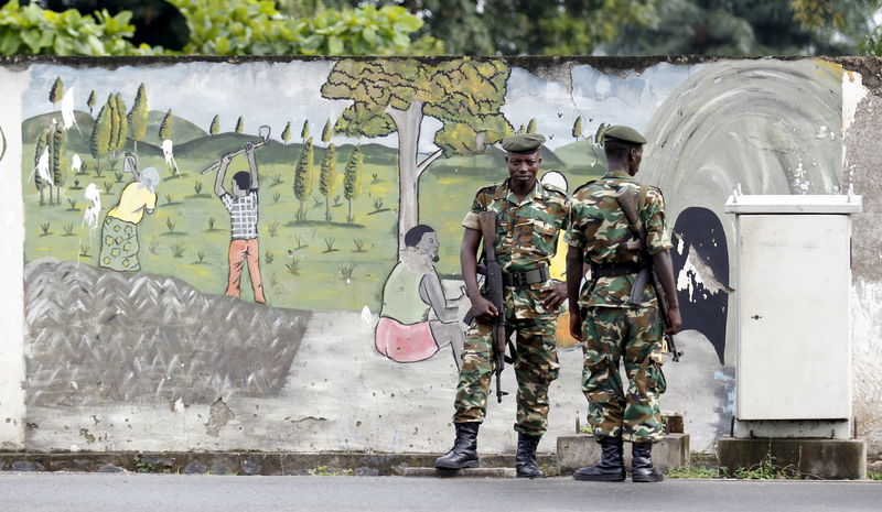 © Reuters. Military officers stand guard near a wall mural showing people working in farms following recent clashes between protesters and riot police as it is used to block a main street in Burundi's capital Bujumbura