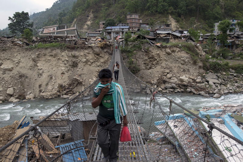 © Reuters. Local residents walk on a bridge, past collapsed buildings, after Tuesday's earthquake at Singati Village