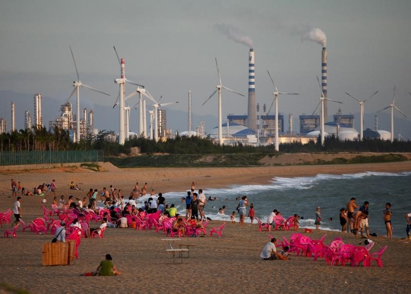 © Reuters. Windmills and a power plant can be seen in the distance as beachgoers watch sunset in the city of Dongfang on the western side of China's island province of Hainan
