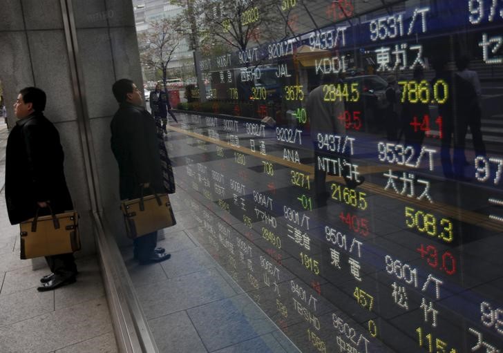 © Reuters. A man hides from the rain in front of an electronic stock quotation board outside a brokerage in Tokyo