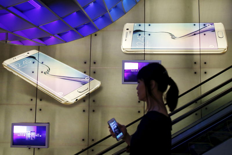 © Reuters. A woman holding an Apple iPhone passes a Samsung Galaxy S6 advertisement at a mall in Singapore