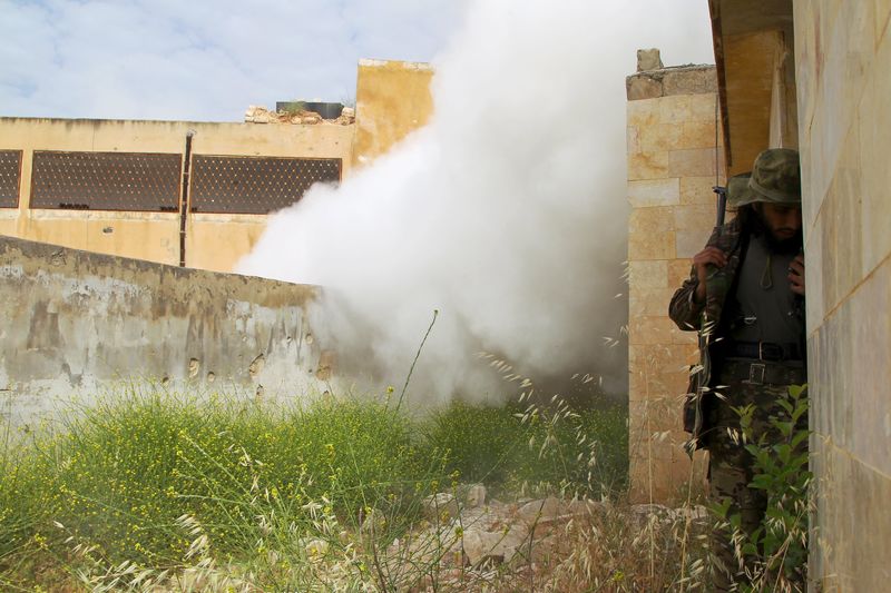 © Reuters. Combatente ao lado de um prédio enquanto fumaça se levanta do local onde caiu um morteiro, em Idlib