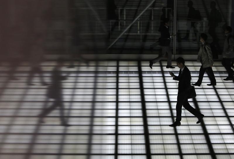 © Reuters. A man with his mobile phone walking is reflected in a wall of a building at Tokyo's business district