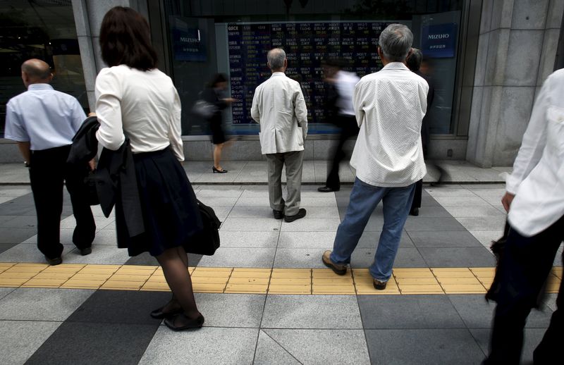 © Reuters. Pedestrians look at an electronic board showing the various stock prices outside a brokerage in Tokyo