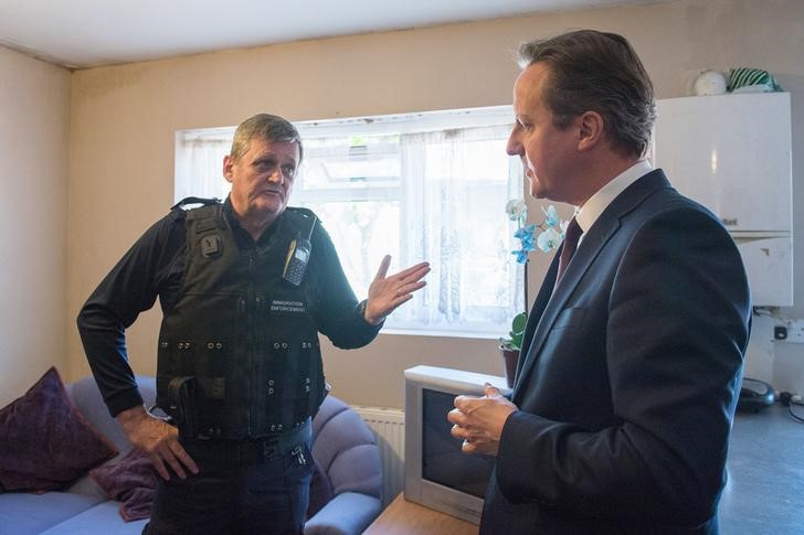 © Reuters. Premiê britânico David Cameron conversa com agente de controle de imigração John Keane após ação de busca por imigrantes ilegais em Londres