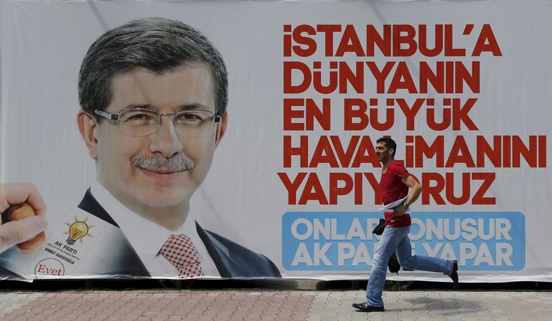 © Reuters. A man runs past by an election billboard with a picture of Turkish Prime Minister Davutoglu is pictured in Istanbul's financial district of Gayrettepe, Turkey