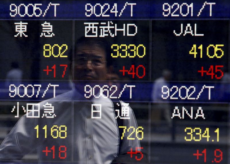 © Reuters. A pedestrian is reflected in an electronic board showing the various stock prices outside a brokerage in Tokyo
