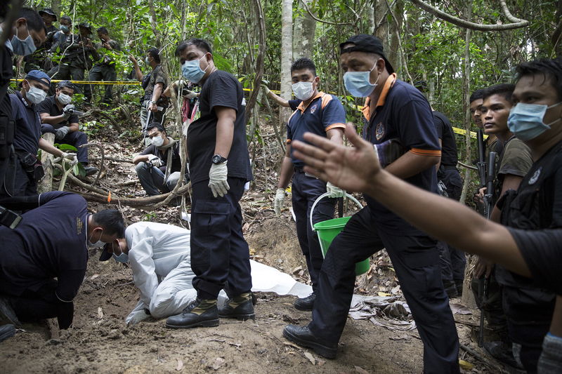© Reuters. Policemen monitor as forensic experts dig out human remains near the abandoned human trafficking camp in the jungle close the Thailand border at Bukit Wang Burma in northern Malaysia