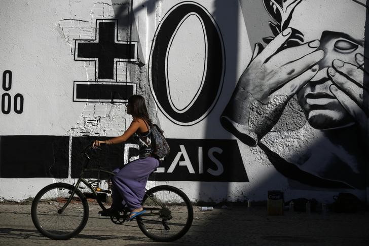 © Reuters. A woman rides her bicycle past a graffiti mocking the Brazilian currency note, the real, in downtown Rio de Janeiro