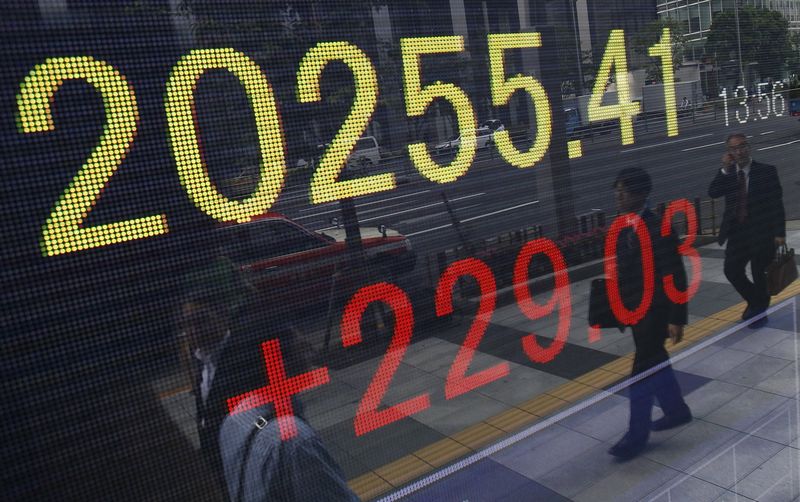 © Reuters. Pedestrians are reflected in an electronic board showing the Japan's Nikkei average outside a brokerage in Tokyo