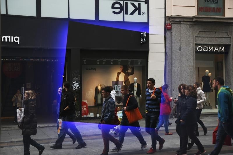 © Reuters. People are reflected in the window of a store as they stroll and shop at a commercial district in central Madrid