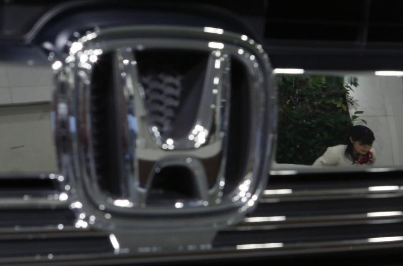 © Reuters. A staff of Honda Motor Co's showroom bows to a visitor as she is reflected in a company logo on a car displayed at company showroom in Tokyo