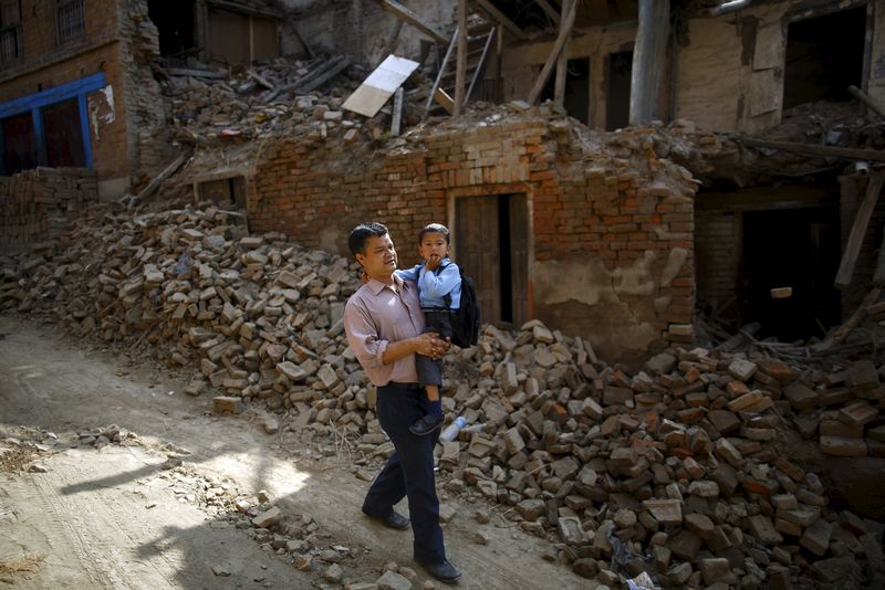 © Reuters. Birendra Karmacharya carries his son Saksham as they walk past the debris of collapsed houses while heading towards the school in Bhaktapur