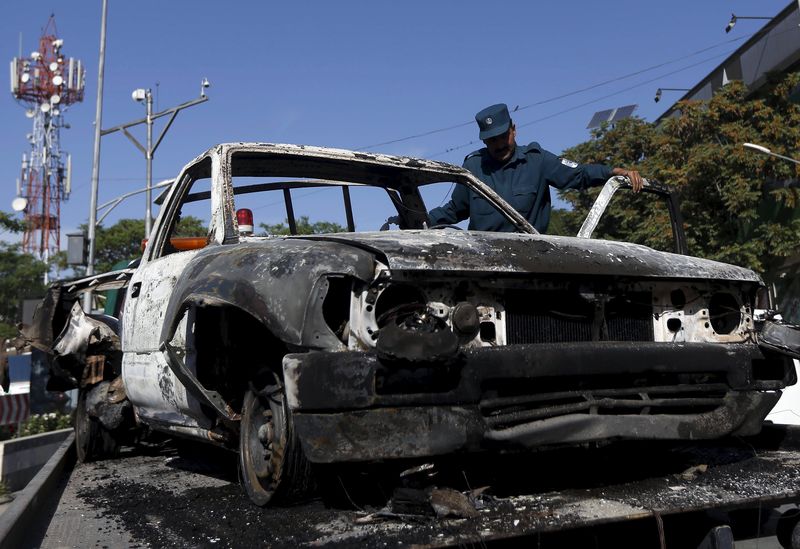 © Reuters. Afghan policeman inspects the wreckage of a car after Taliban attack on a guesthouse in Kabul 