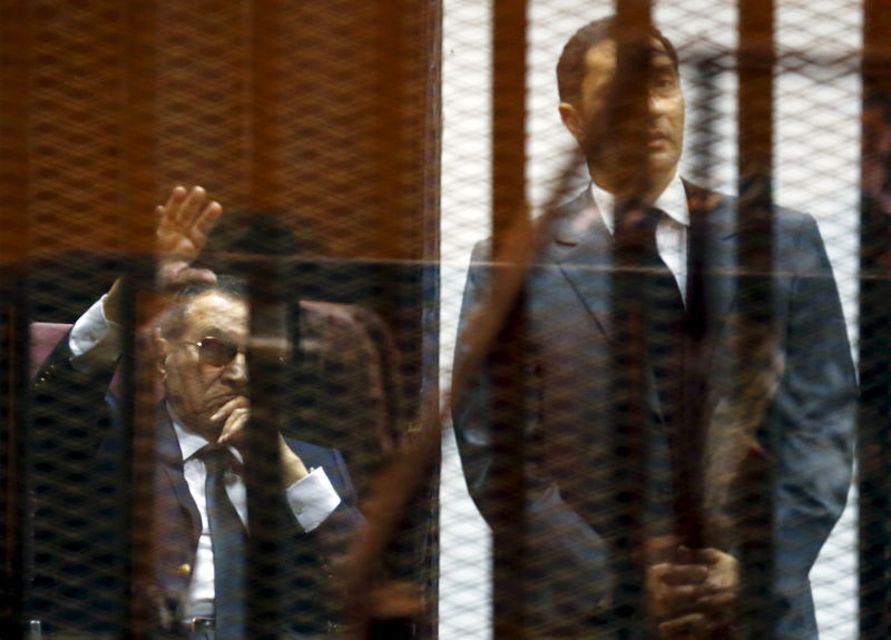 © Reuters. Egypt's former president Hosni Mubarak waves to his supporters with his sons Alaa and Gamal inside a cage in a courtroom during their trial at the police academy, on the outskirts of Cairo