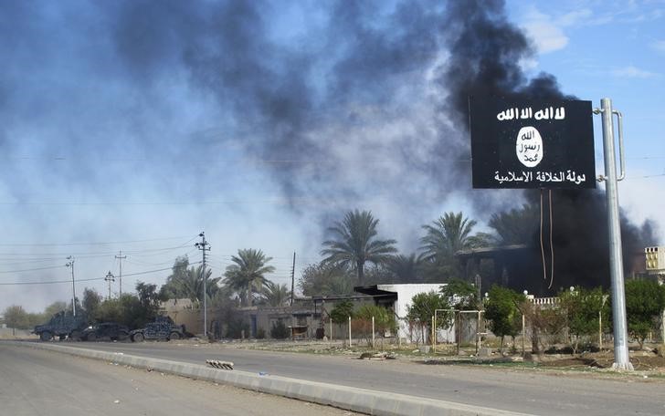 © Reuters. Smoke raises behind an Islamic State flag after Iraqi security forces and Shiite fighters took control of Saadiya from Islamist State militants