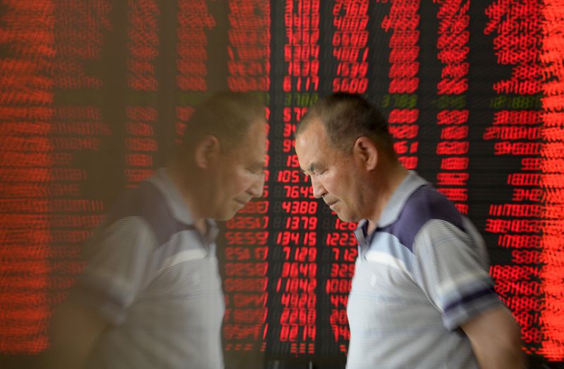 © Reuters. An investor is reflected on the surface of a wall as he walks past an electronic board showing stock information, filled with red figures indicating rising prices, at a brokerage house in Taiyuan