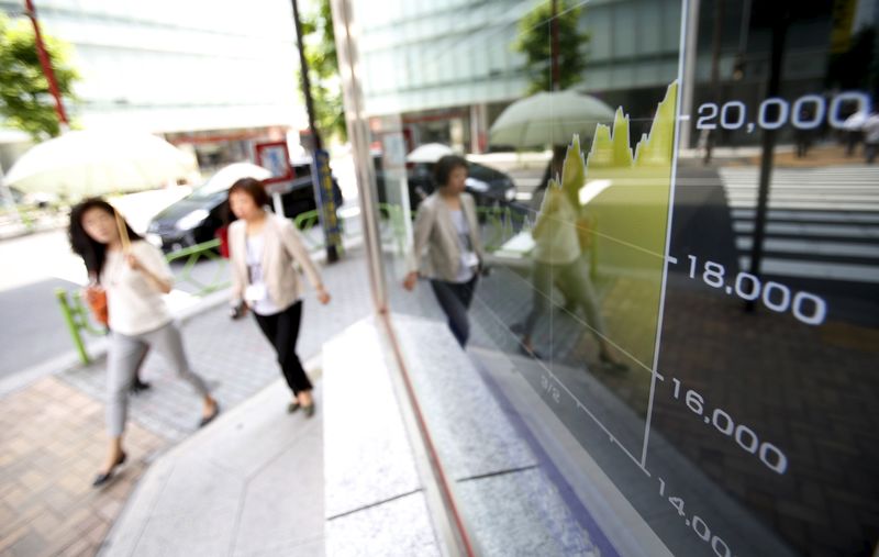 © Reuters. Pedestrians walk next to an electronic board showing the graph of the recent fluctuations of the Japan's Nikkei average outside a brokerage in Tokyo