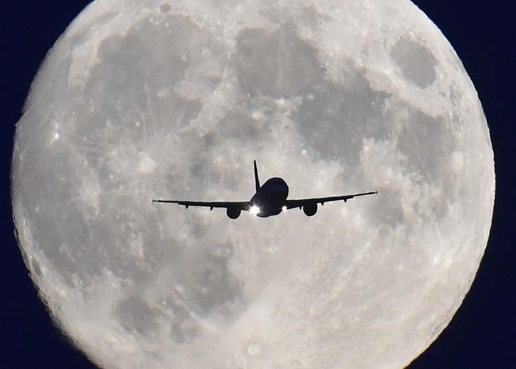 © Reuters. A passenger plane passes in front of the full moon as it makes a final landing approach to Heathrow Airport in west London