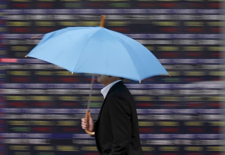 © Reuters. A man holding an umbrella walks in front of an electronic stock quotation board outside a brokerage in Tokyo