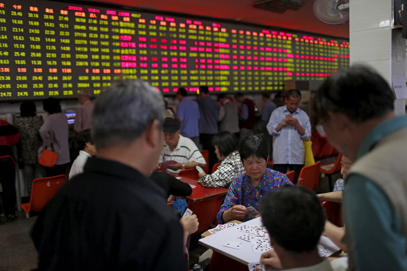 © Reuters. Investors play cards in front of a screen showing stock information at a brokerage house in Shanghai