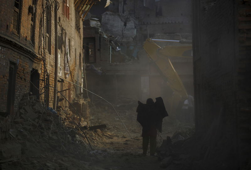 © Reuters. A woman covers herself with a shawl as dust blows while the wreckage of a house damaged in an earthquake is demolished in Bhaktapur