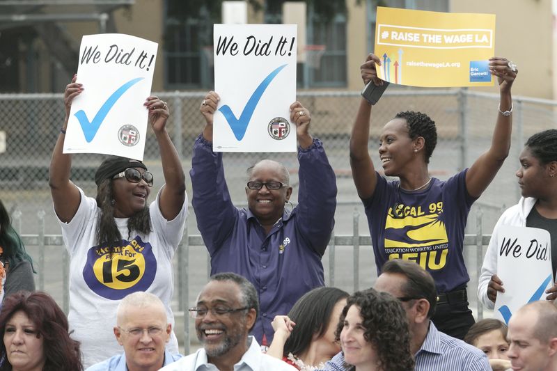 © Reuters. People hold up signs at a celebration event for the signing of an ordinance raising the city's minimum wage in Los Angeles