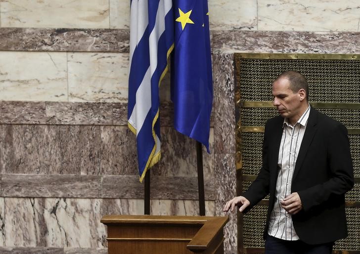 © Reuters. Greek Finance Minister Varoufakis walks next to an EU and a Greek national flag during a parliamentary session in Athens 