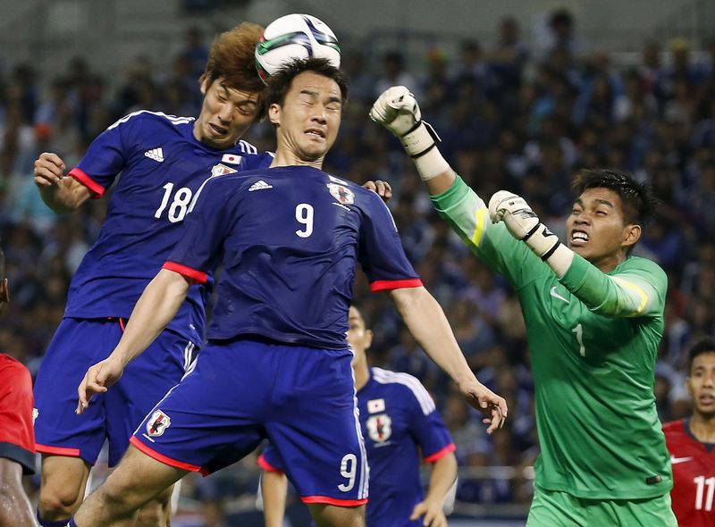 © Reuters. Singapore's goalkeeper Izwan Mahbud fights for the ball with Japan's Shinji Okazaki and Yuya Osako during their 2018 World Cup qualifying soccer match at Saitama Stadium in Saitama