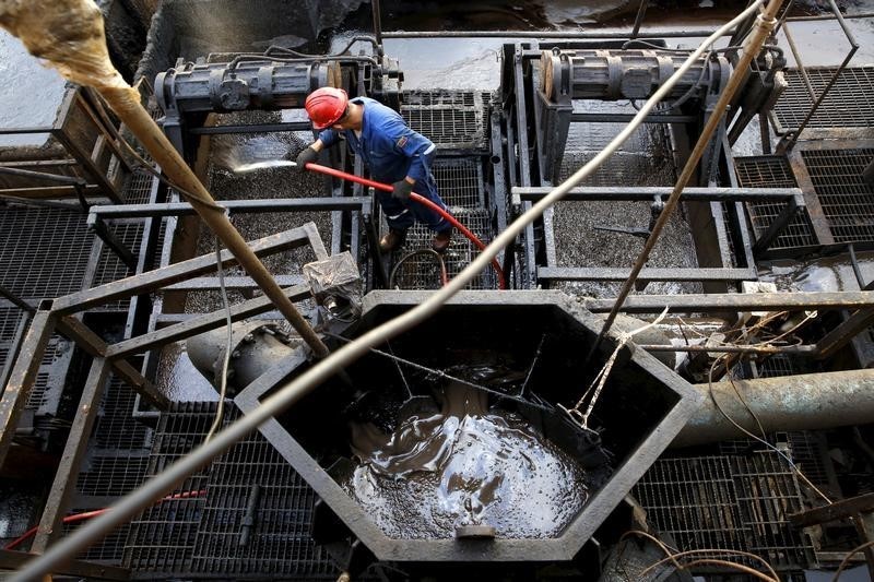 © Reuters. The flow of crude oil is seen in a container while an oilfield worker works on a drilling rig at an oil well operated by Venezuela's state oil company PDVSA, in the oil rich Orinoco belt, near Cabrutica at the state of Anzoategui