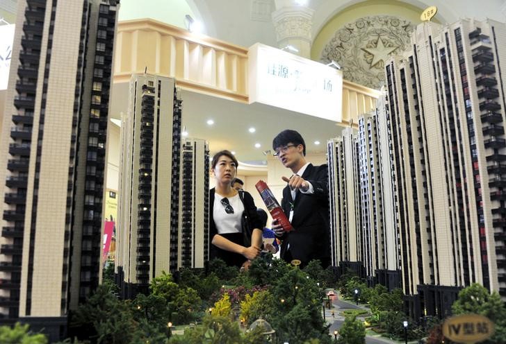 © Reuters. A sales assistant speaks to a customer in front of a model of a residential complex, at a real estate exhibition in Shanghai