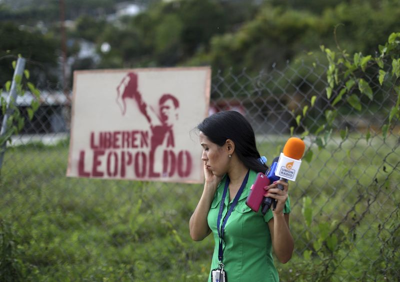 © Reuters. Jornalista fala ao celular diante de um cartaz pedindo a libertação do líder opositor Leopoldo López