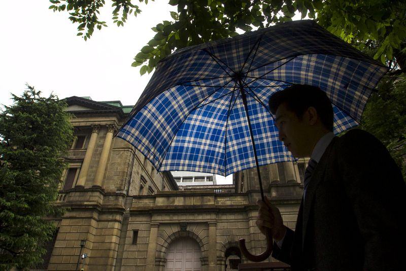 © Reuters. Man holds umbrella as they walk past BOJ building on rainy day in Tokyo 