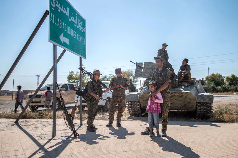 © Reuters. Fighters of the Kurdish People's Protection Units stand with children near a sign in Tel Abyad town