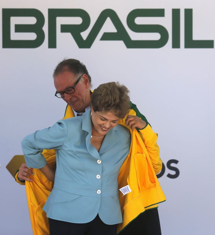 © Reuters. Presidente do comitê organizador da Olimpíada de 2016, Carlos Arthur Nuzman (atrás), ajuda a presidente Dilma Rousseff a colocar o agasalho da equipe brasileira durante comemoração do Dia Olímpico, no Rio de Janeiro