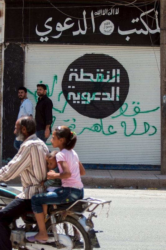 © Reuters. Civis em uma moto passam em frente a um escritório que pertenceu a combatentes do Estado Islâmico, em Tel Abyad