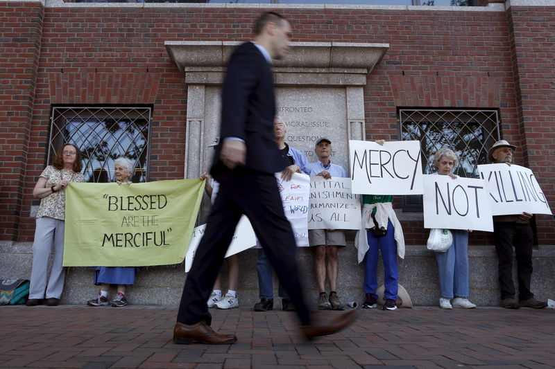 © Reuters. A pedestrian walks past death penalty protesters before the formal sentencing of convicted Boston Marathon bomber Dzhokhar Tsarnaev at the federal courthouse in Boston