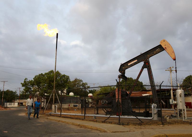 © Reuters. Two people walk past an oil pump in Lagunillas, Ciudad Ojeda