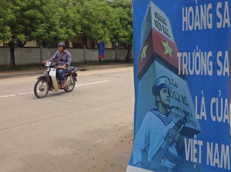 © Reuters. A man rides a motorcycle past a poster promoting Vietnam' sovereignty in the East Sea on Phu Quoc island