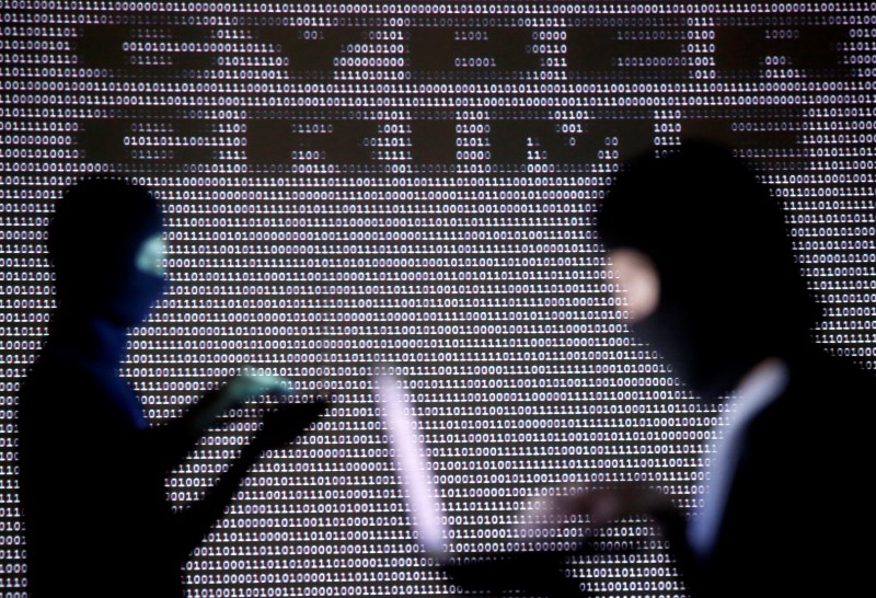 © Reuters. Picture illustration of People posing with laptops in front of projection with word 'cyber' and binary code in Zenica 