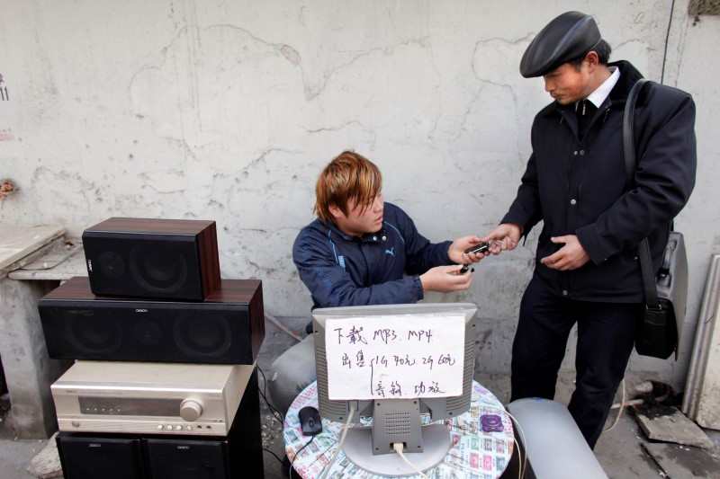 © Reuters. A man returns a cell phone to a customer after downloading music onto it at a street stand in Shanghai