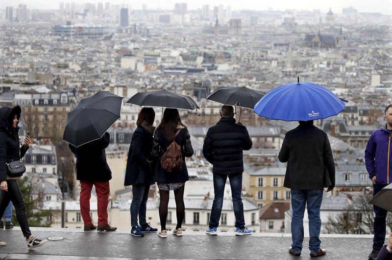 © Reuters. Tourists hold umbrellas at Butte Montmartre overlooking Paris